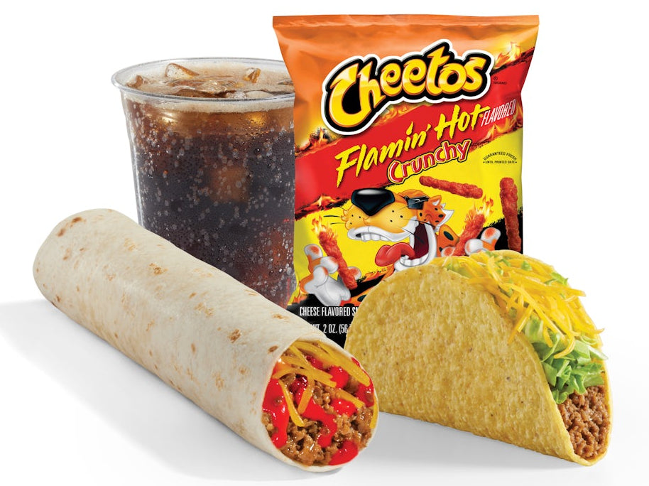 A Cheetos Flamin' Hot Candy snack bag standing behind a burrito and a taco, with a cup of ice cold cola.